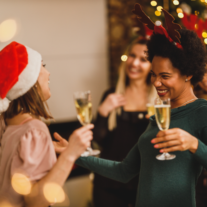 Women holding champagne flutes and wearing Christmas-themed headpieces